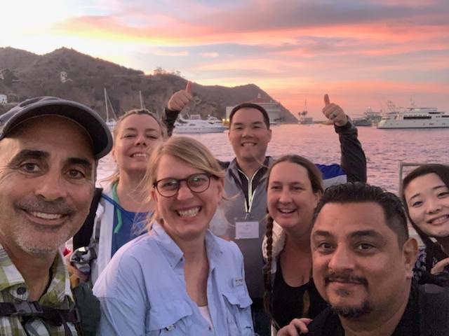 Seven faculty take a group selfie with sunset behind them