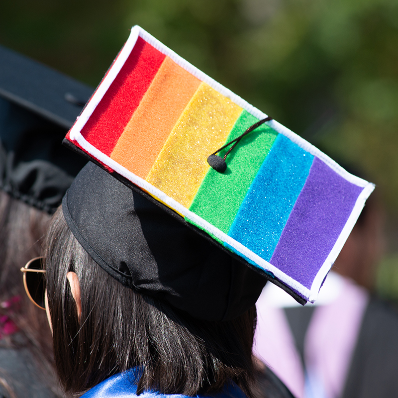 A graduation student shows off a rainbow grad cap at commencement.