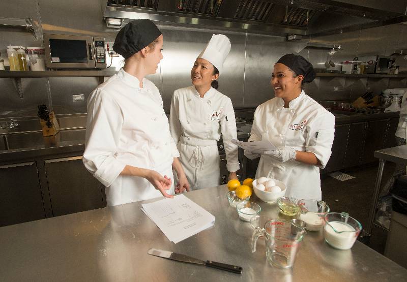 A professor discusses culinary management with students in their kitchen laboratory. A professor discusses culinary management with students in their kitchen laboratory.