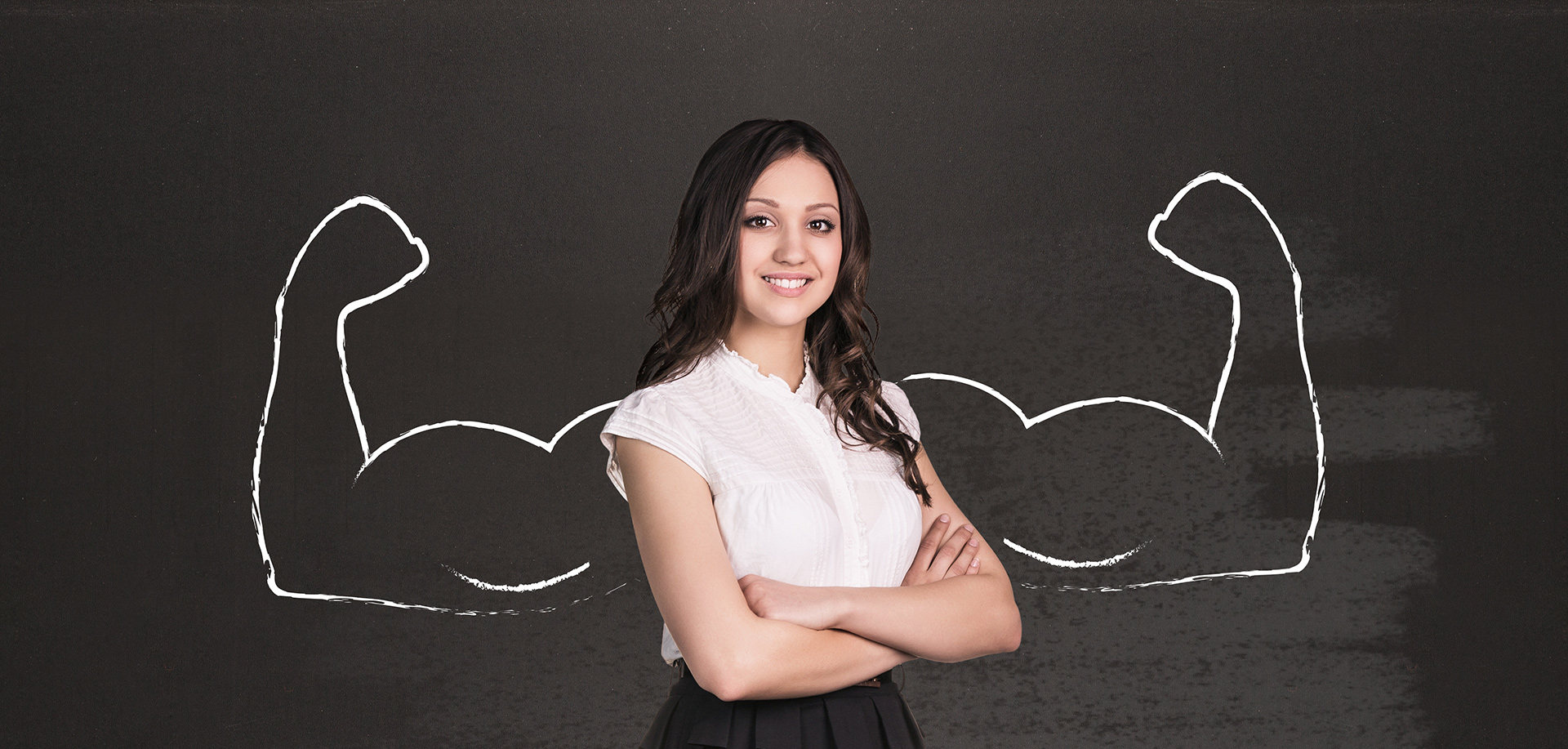 A photo of a young woman standing in front of a chalkboard with muscles drawn behind her