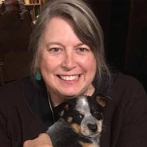 A woman smiling and looking into the camera while holding a puppy