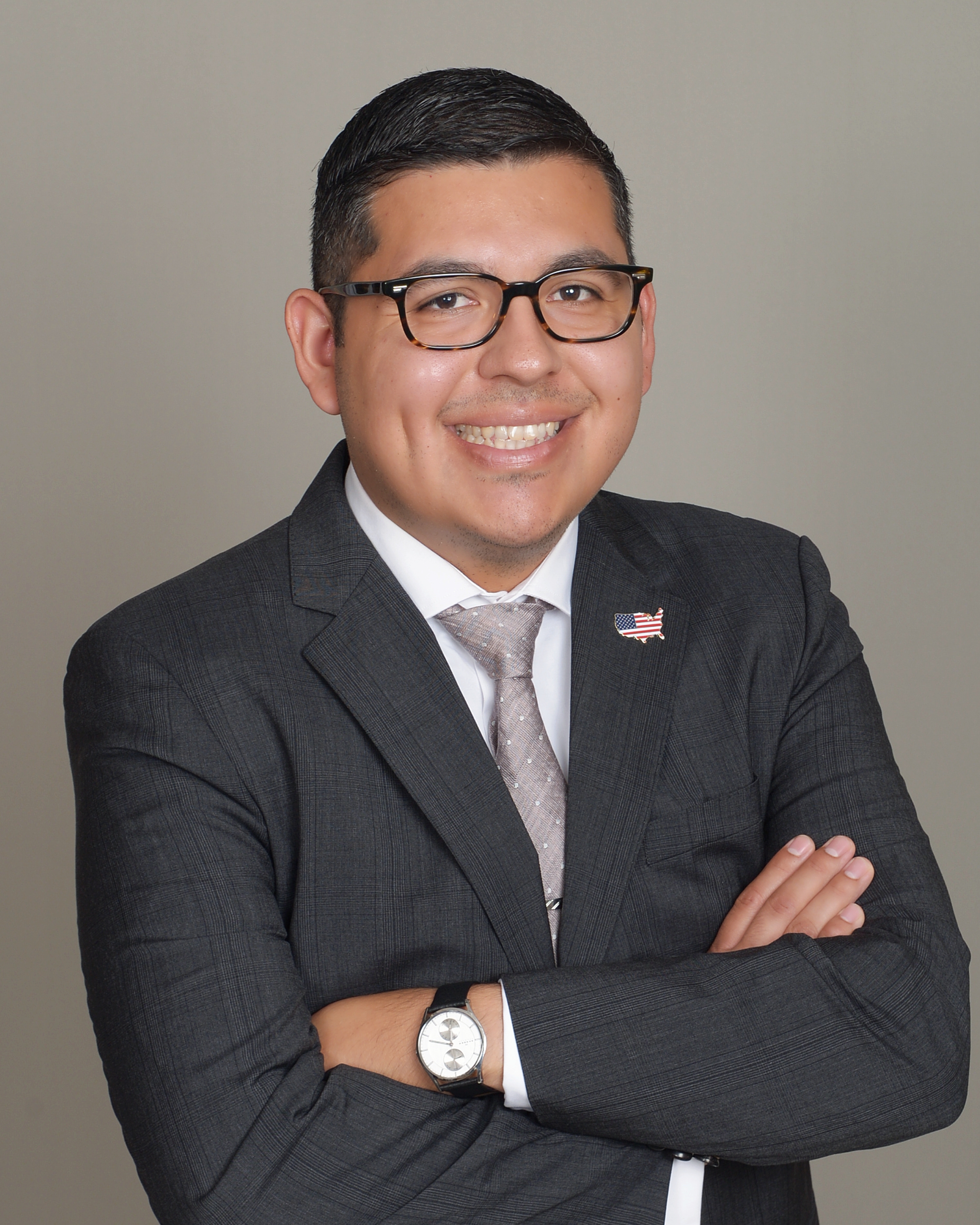 Raul Madrid smiling, wearing a suit, with arms folded