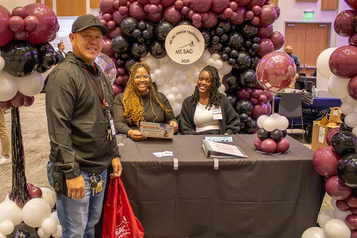 Three people pose for a photo at a booth at a Reverse Vendor Trade Show at Mt. SAC.