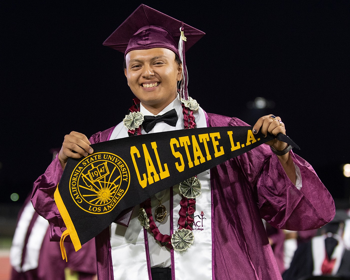 A student at graduation holding a Cal State L.A. pennant. 