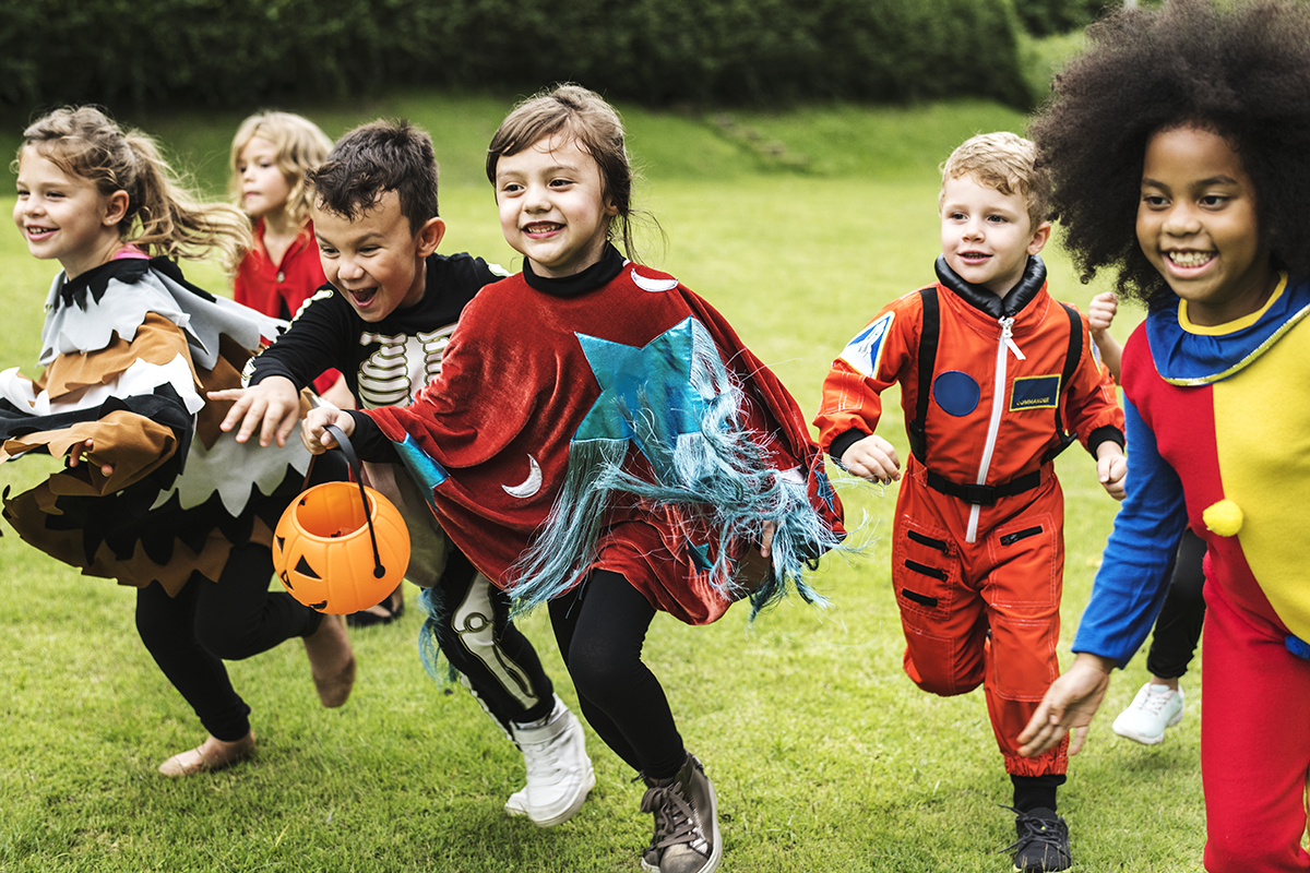 A group of young children in Halloween costumes race across a field to secure treats.