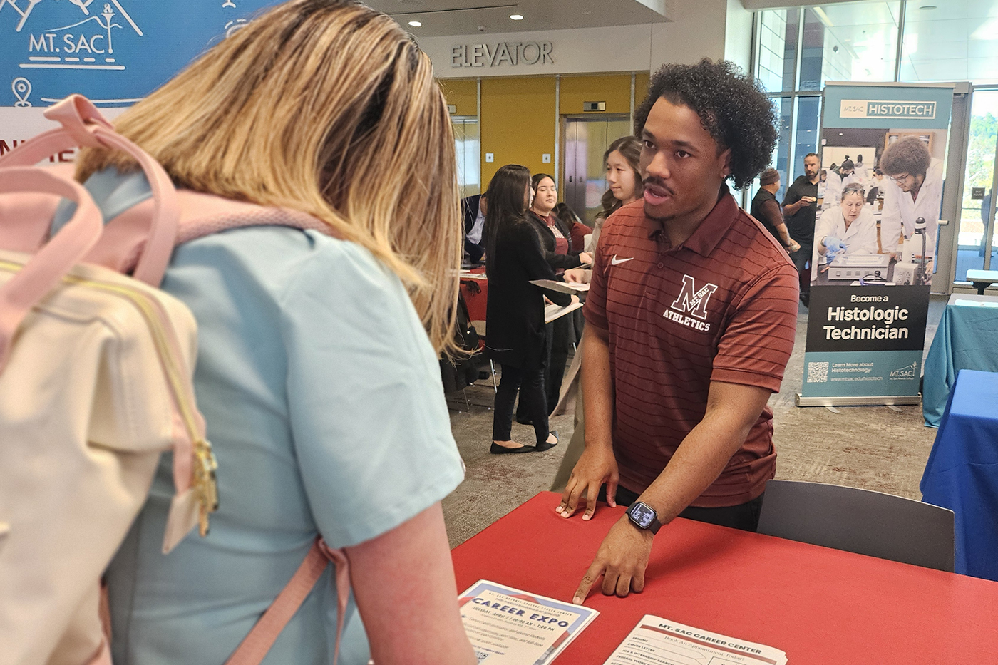 A volunteer informs an interested guest about the upcoming Career Expo.