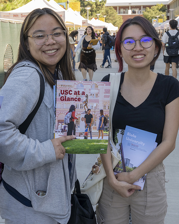 Students hold up college information at an on-campus event. 
