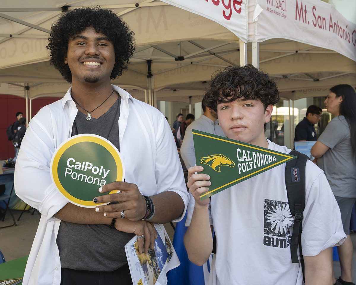Students hold up Cal Poly Pomona college information at an event.
