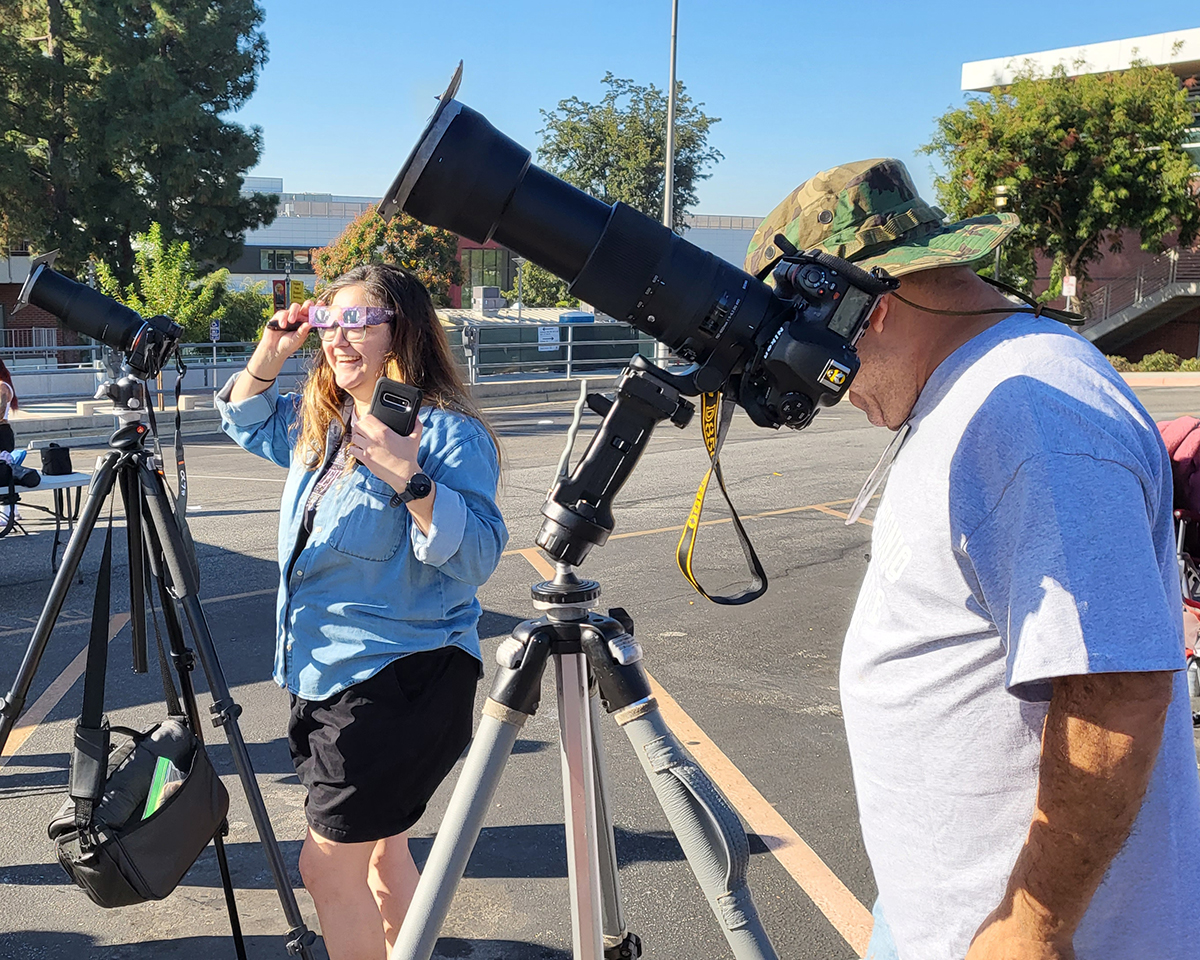 Adults on campus using telescopes to look at an eclipse. 