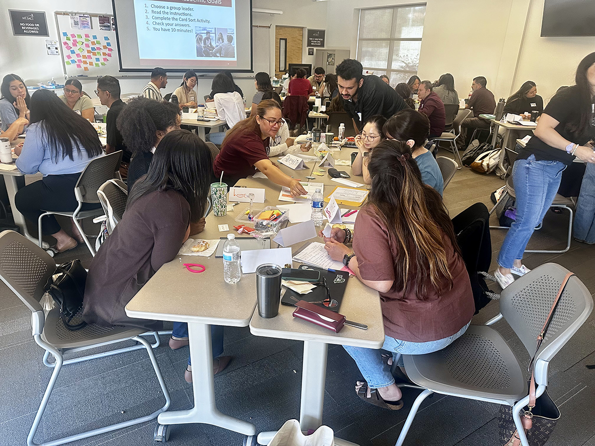 A group of students gather around a table to learn from a counselor during a summer class. 
