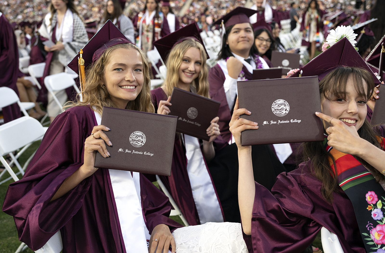 A group of students smile and hold up their diplomas at graduation.