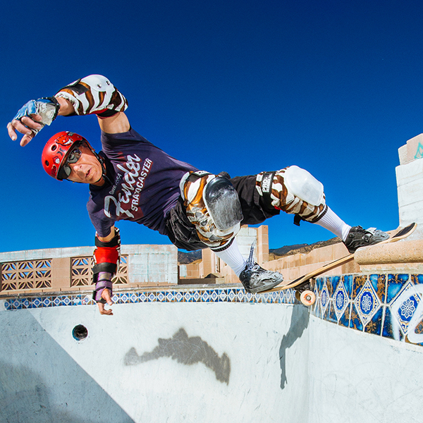 A skateboarder lands a trick on the lip of an empty pool. 