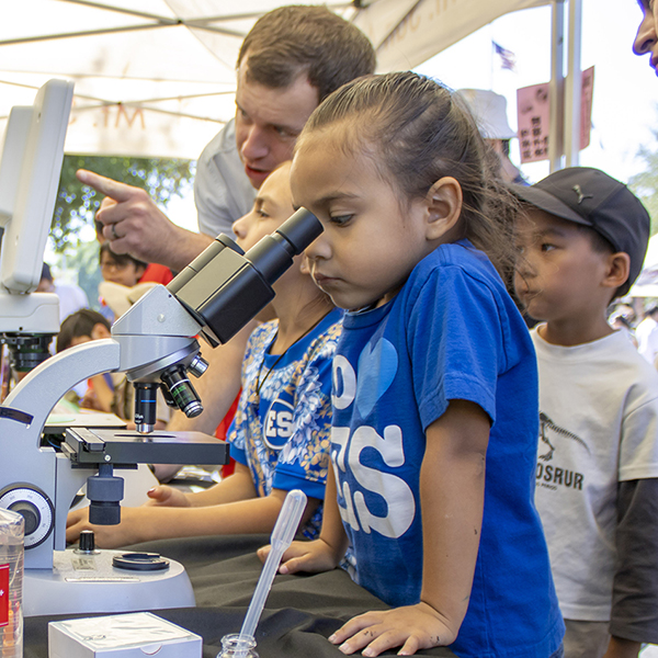 A young child looks through the lenses of a microscope at the Family Science Festival at Mt. SAC.
