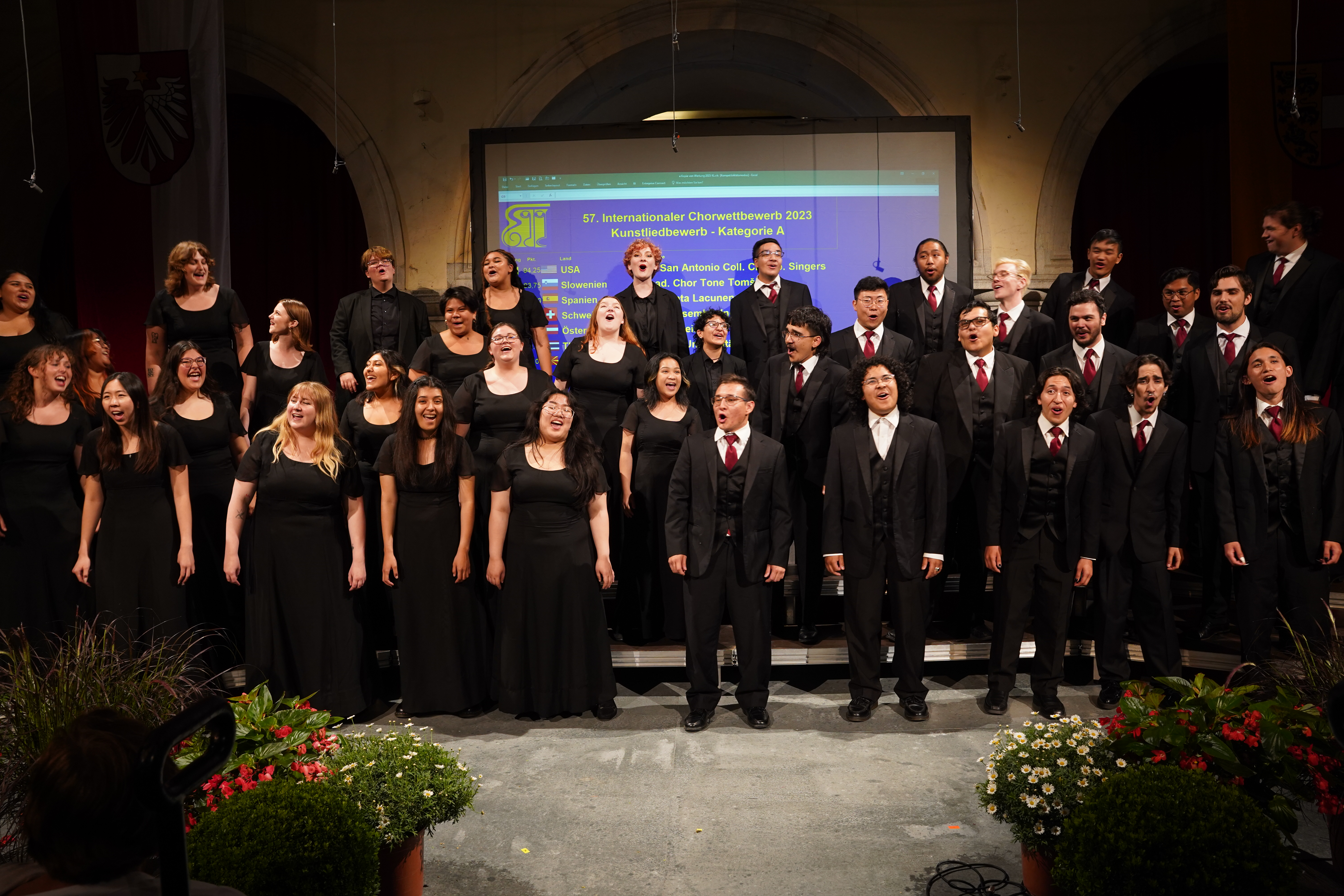 Large group of singers perform while dressed formally