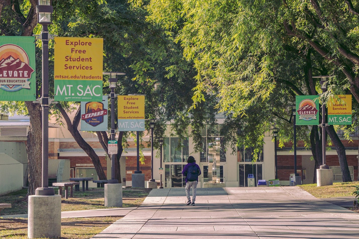 Student with backpack walks toward Clarke Theatre along tree-lined path