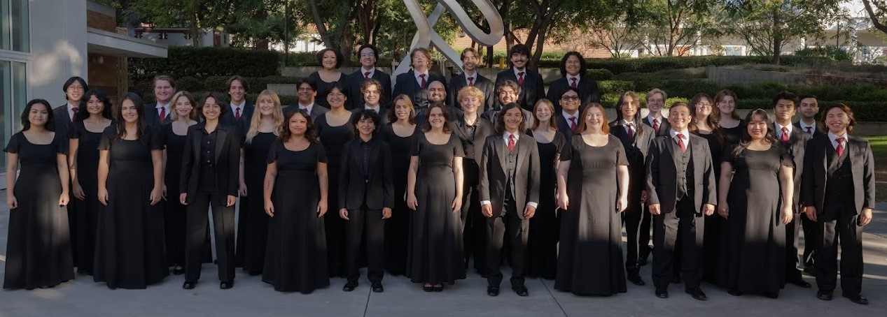 Large group of singers pose in front of statue while dressed formally