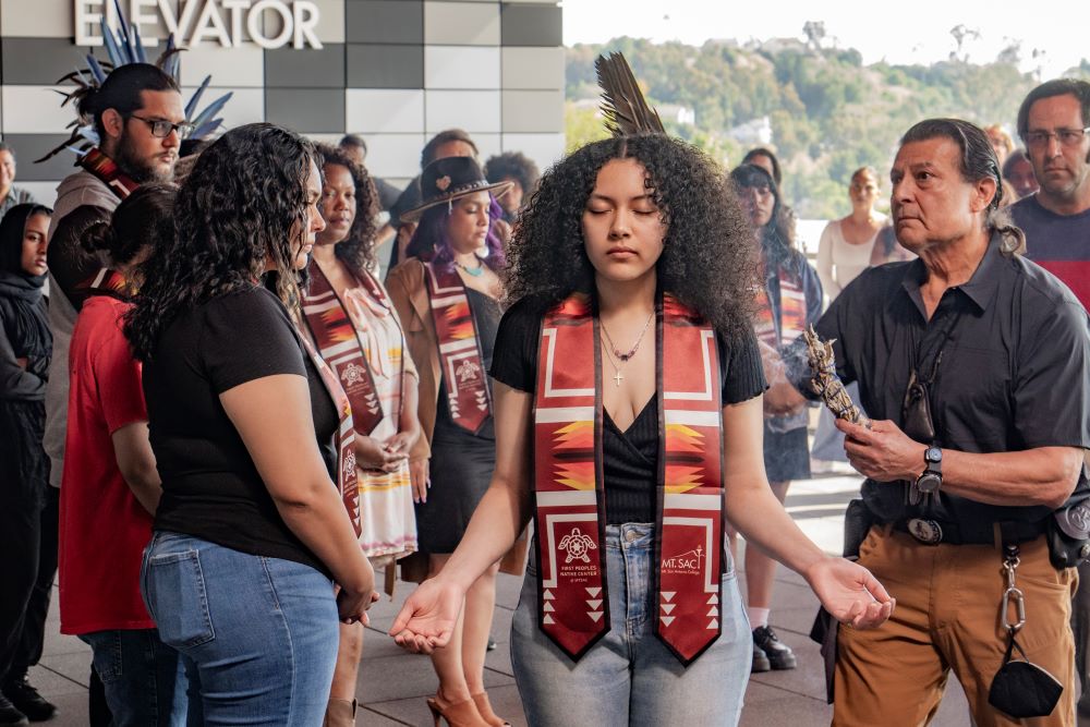 Student stands with arms stretched before as she is blessed with sage