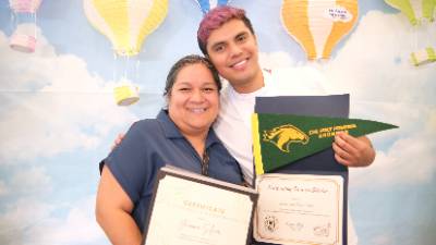 A young man with pink hair and a woman display certificates celebrating transfer and also a Cal Poly Pomona green and yellow pennant