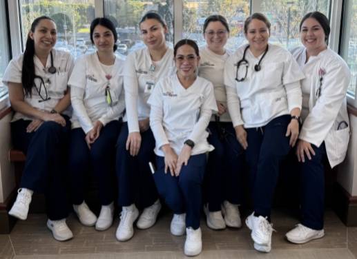 A group of women wearing white nursing tops looking at the camera.