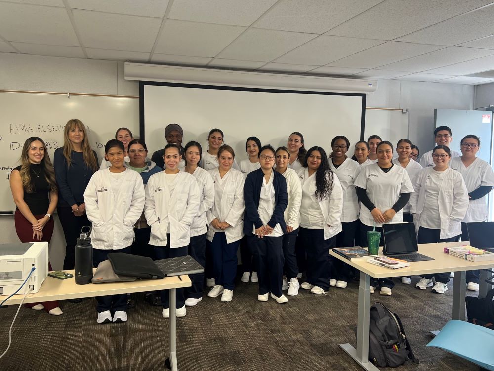 A large group of nursing students dressed in white scrub tops and their professors smile at camera.