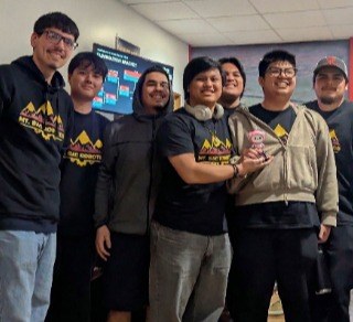 Male members of the robotics team pose with a pink toy robot