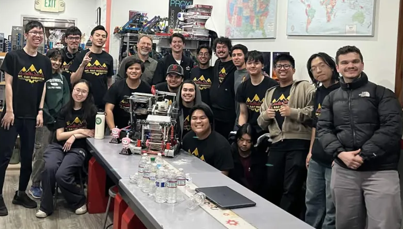 A group of male and female students posing with a robot they createed