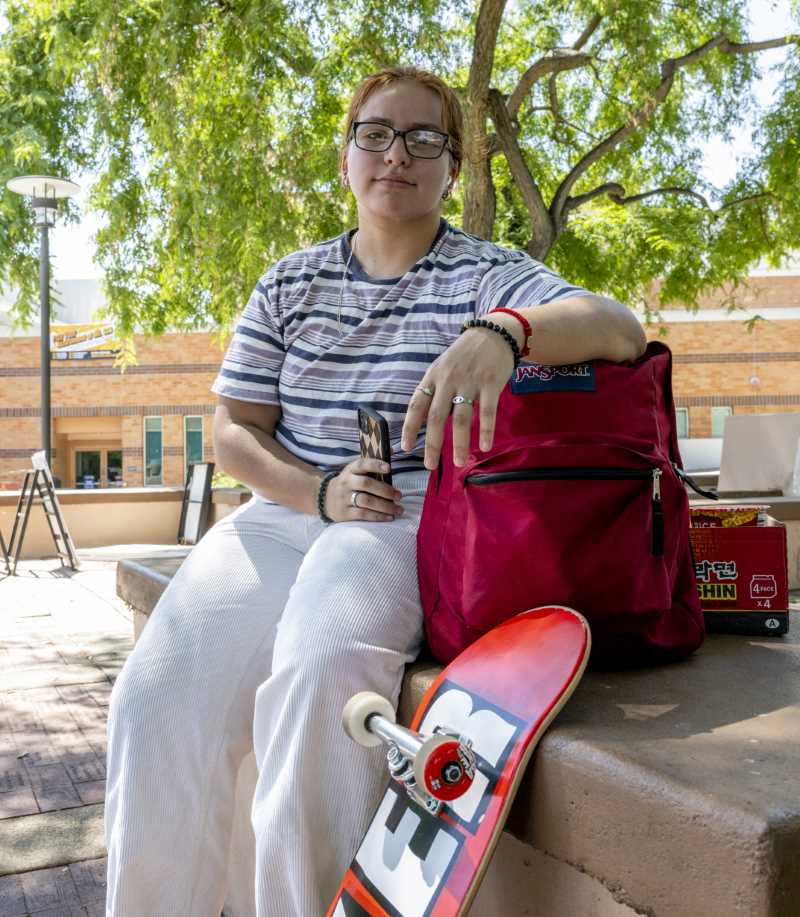 Student with skateboard sits in the shade 