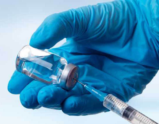 Gloved Hand holds vaccine while syringe draws it 