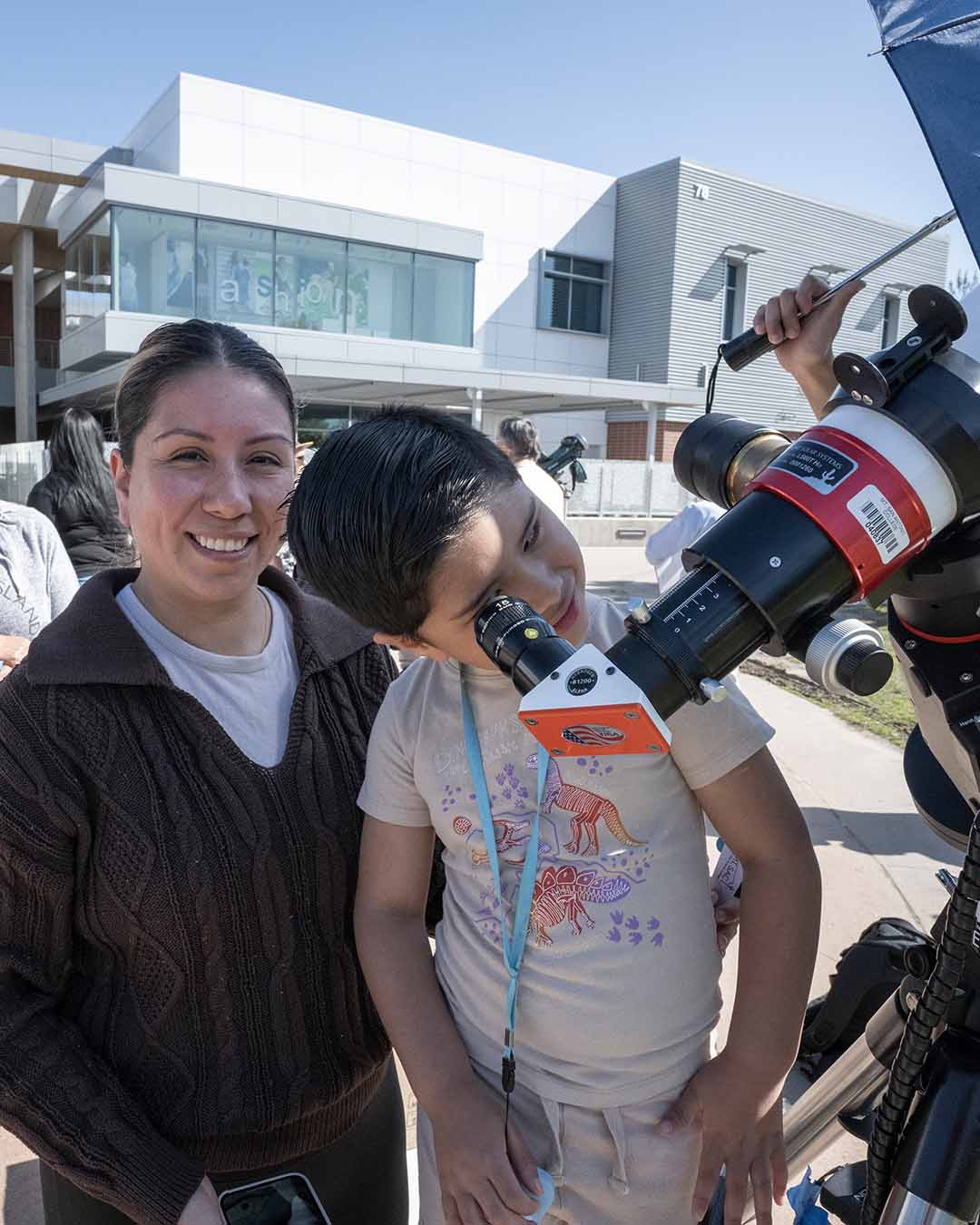 Mom smiles while son looks into telescope