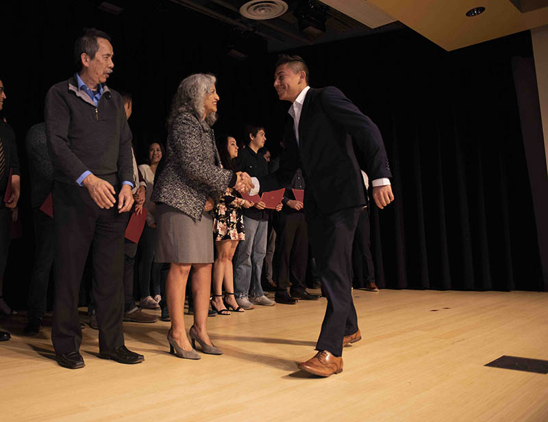 A student (R) is handed their certificate by Gary Chow (L) and Laura Santos (M)