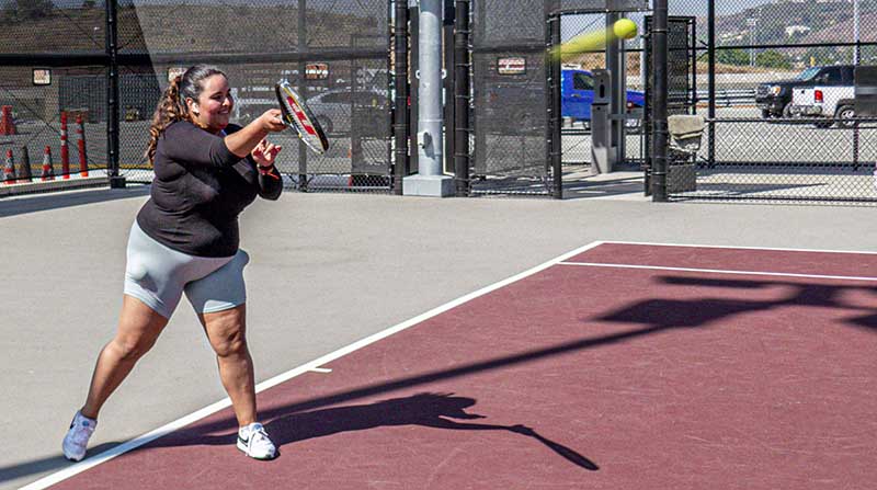 Student hits a tennis ball/ cars parked in background