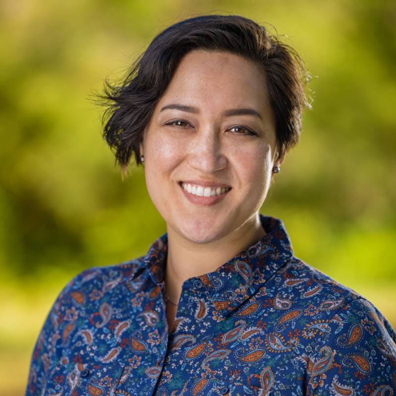 Headshot of Ginger Klee in a blue paisley button up collared shirt with a green background