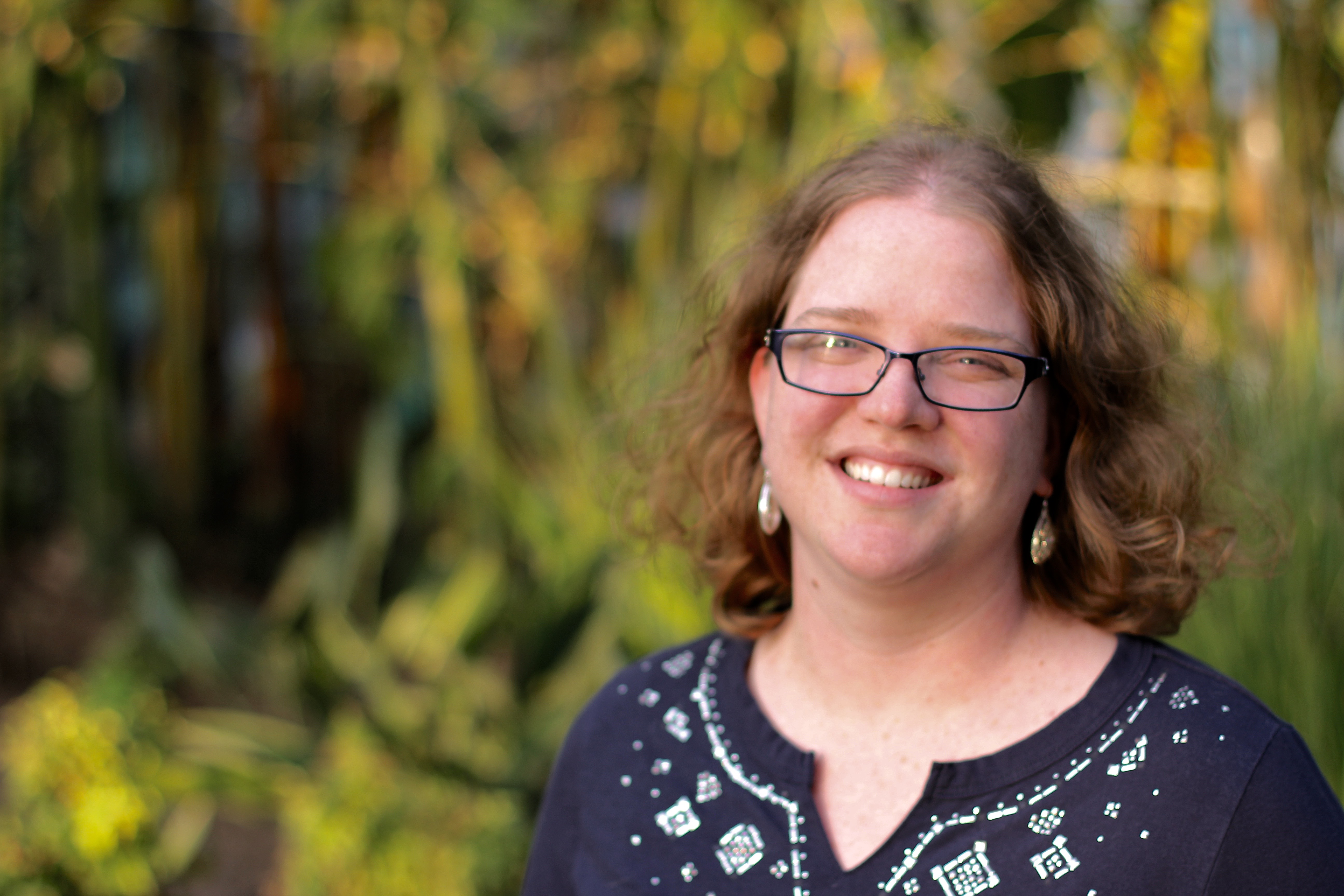 white woman with medium length curly hair, wearing glasses, smiling