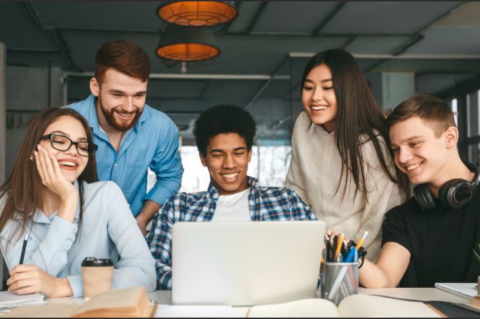 5 youth looking at laptop smiling