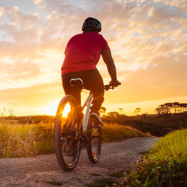 person riding away on bike towards setting sun